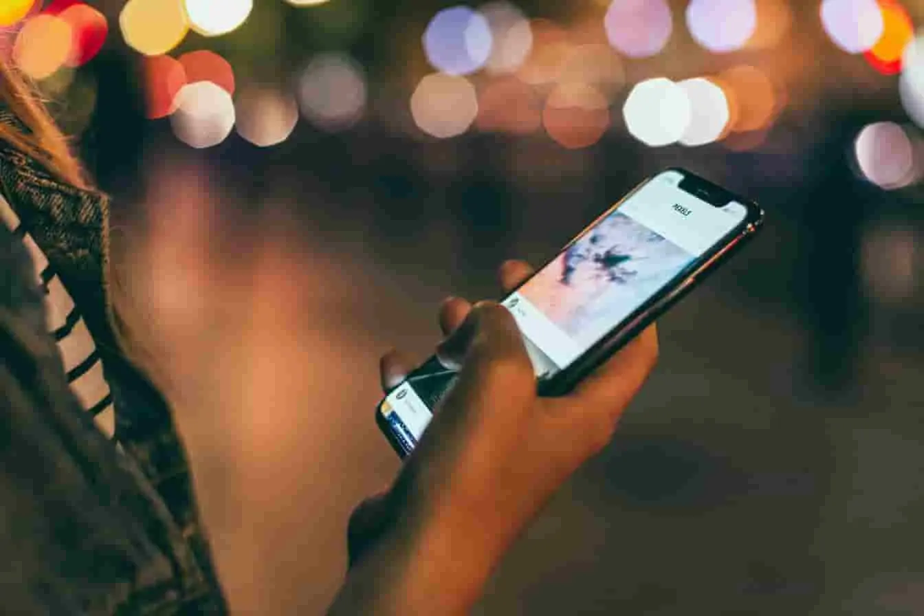 Personne tenant un smartphone affichant une vidéo, ambiance urbaine nocturne, image liée au visionnage et téléchargement de contenu Instagram