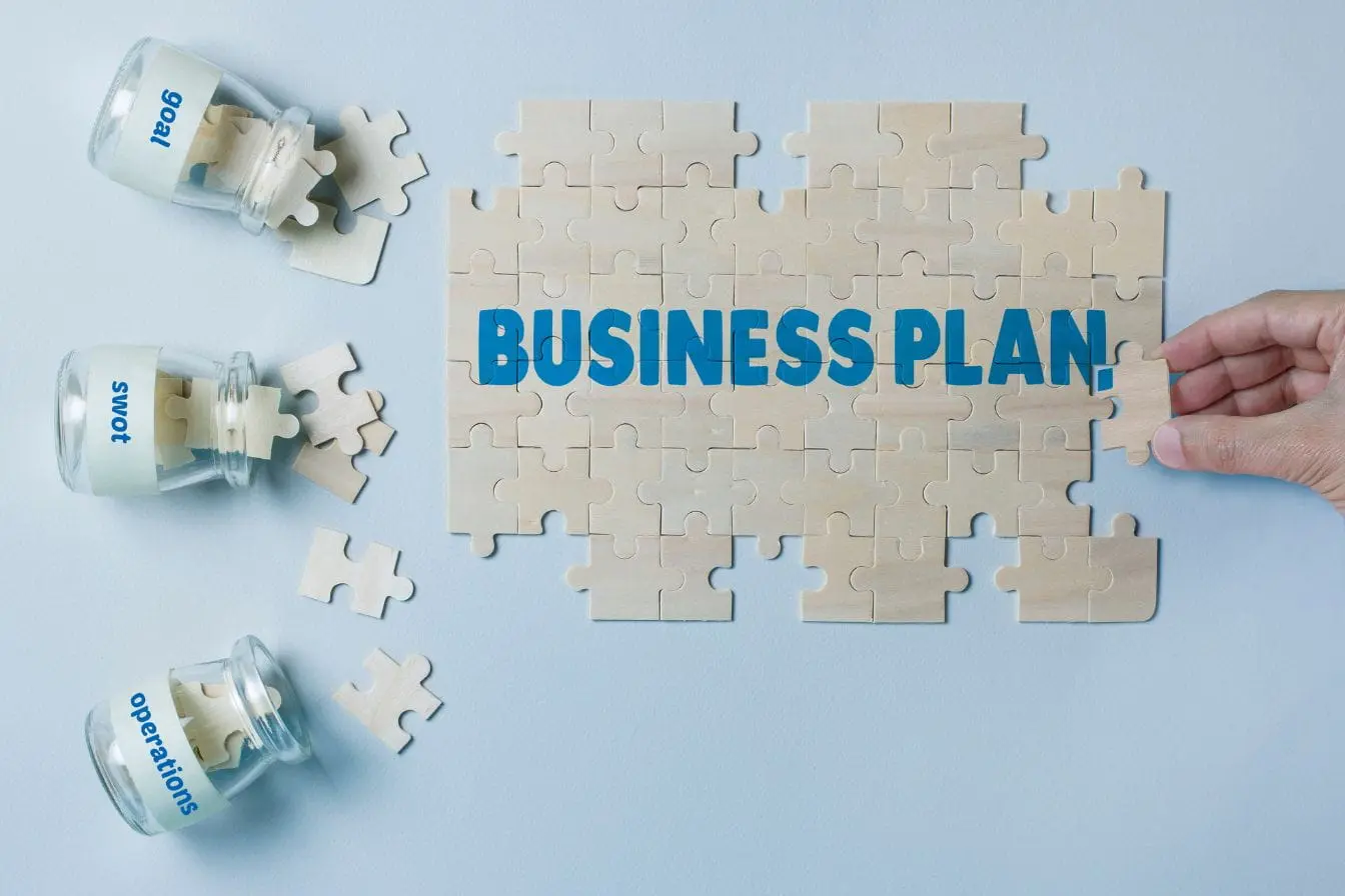 Puzzle affichant business plan complété par une main, image représentant la construction d’un business plan avec objectifs, SWOT et opérations