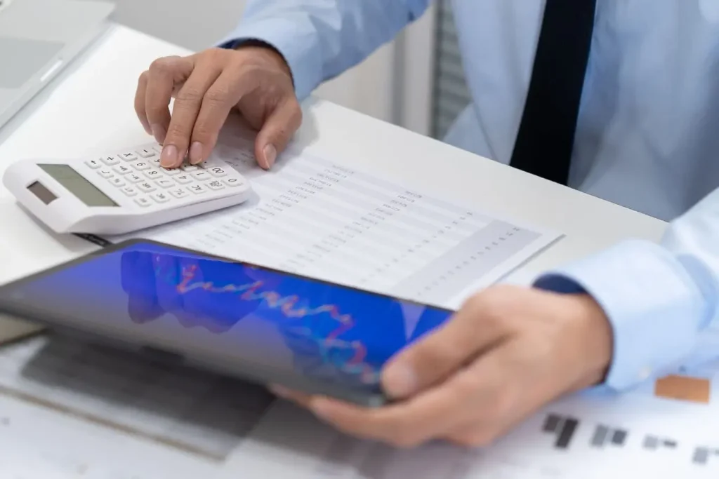 Personne en costume utilisant calculatrice et tablette avec graphiques colorés, image illustrant le churn rate et l’analyse des pertes clients.