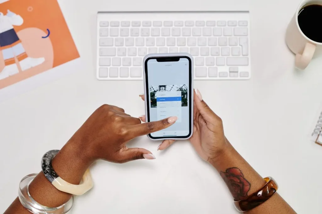 Deux mains éditent une photo sur smartphone posé sur bureau créatif, illustrant la collaboration et l’innovation en co‑marketing digital.