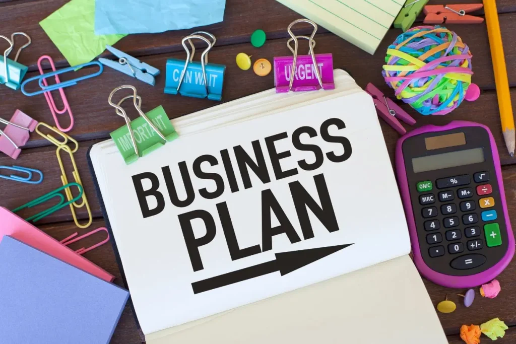 Carnet ouvert affichant business plan entouré de fournitures colorées, image représentant l’organisation et la planification d’un business plan