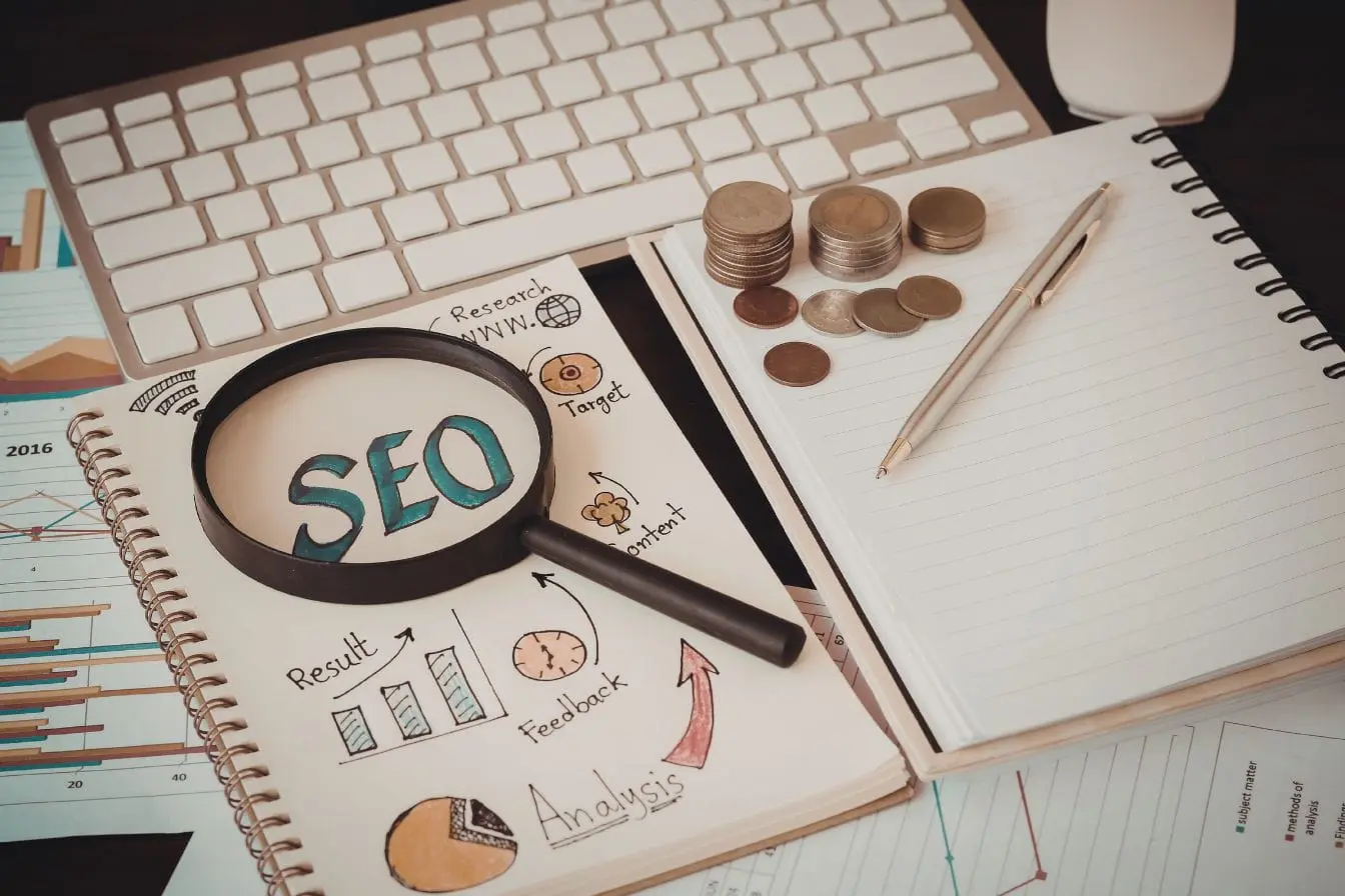 Clavier blanc avec loupe sur carnet SEO, image illustrant la stratégie Rich Snippets pour améliorer visibilité et résultats dans les moteurs de recherche.