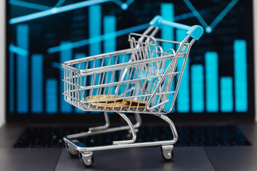 Petit chariot de courses avec pièces dorées sur clavier, représentant l’e-commerce et l’impact psychologique des prix calibrés pour séduire.