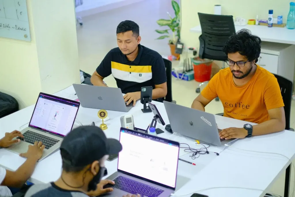 Quatre personnes autour d’une table avec ordinateurs, image illustrant les différences clés entre incubateur et accélérateur pour accompagner une startup.