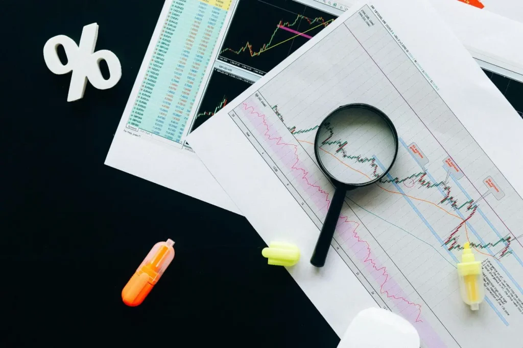 Documents financiers et loupe sur graphiques, image illustrant la Due Diligence et l’analyse minutieuse des données de marché.