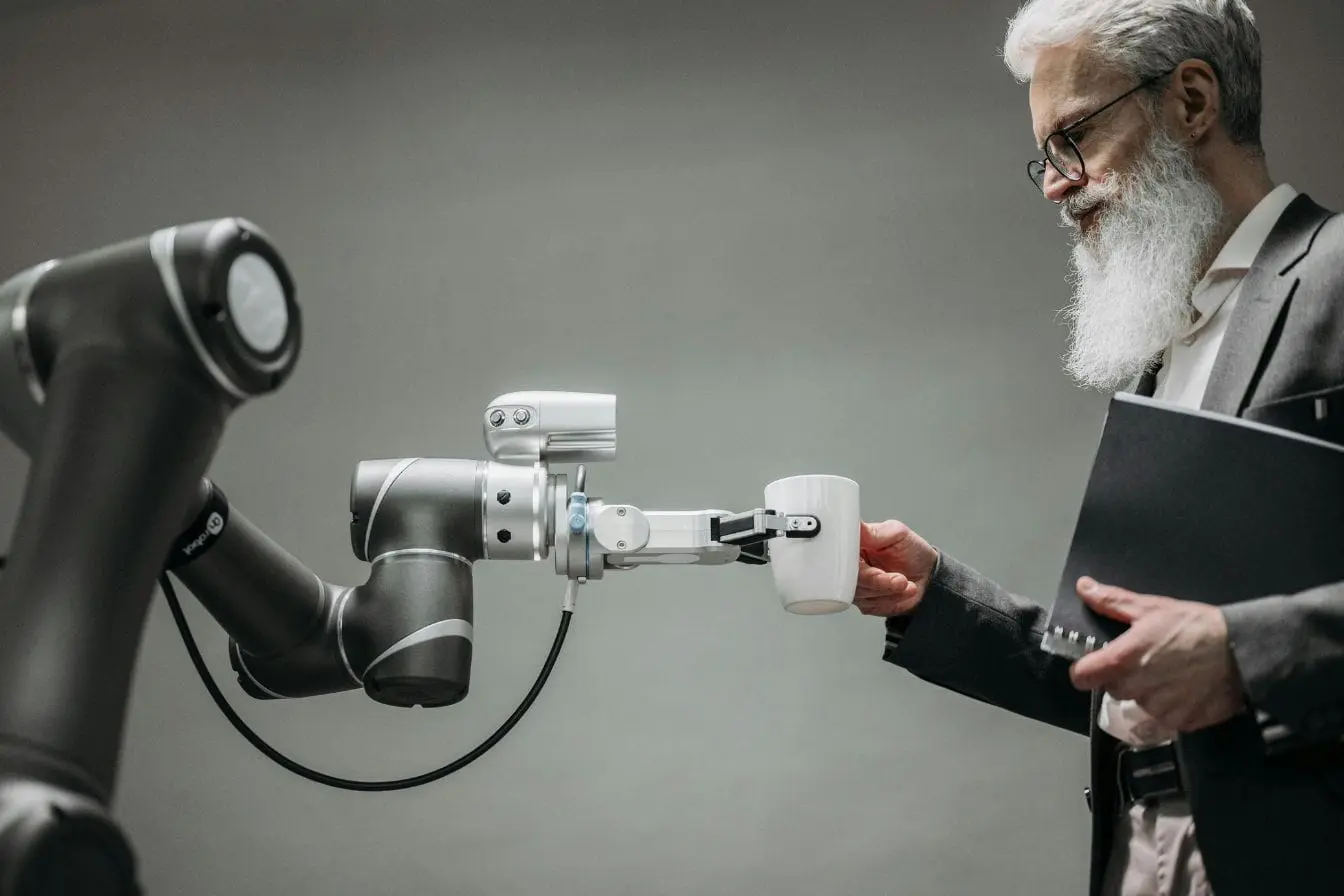 Bras robotique tendant une tasse à un homme barbu en costume, image illustrant la collaboration homme-machine rendue possible par le Machine Learning.