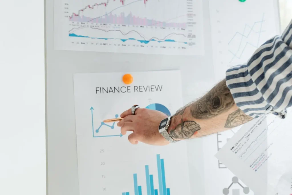 Main tatouée pointant un graphique finance review, image d’un marketing basé sur consentement où le client choisit d’analyser et recevoir l’information.