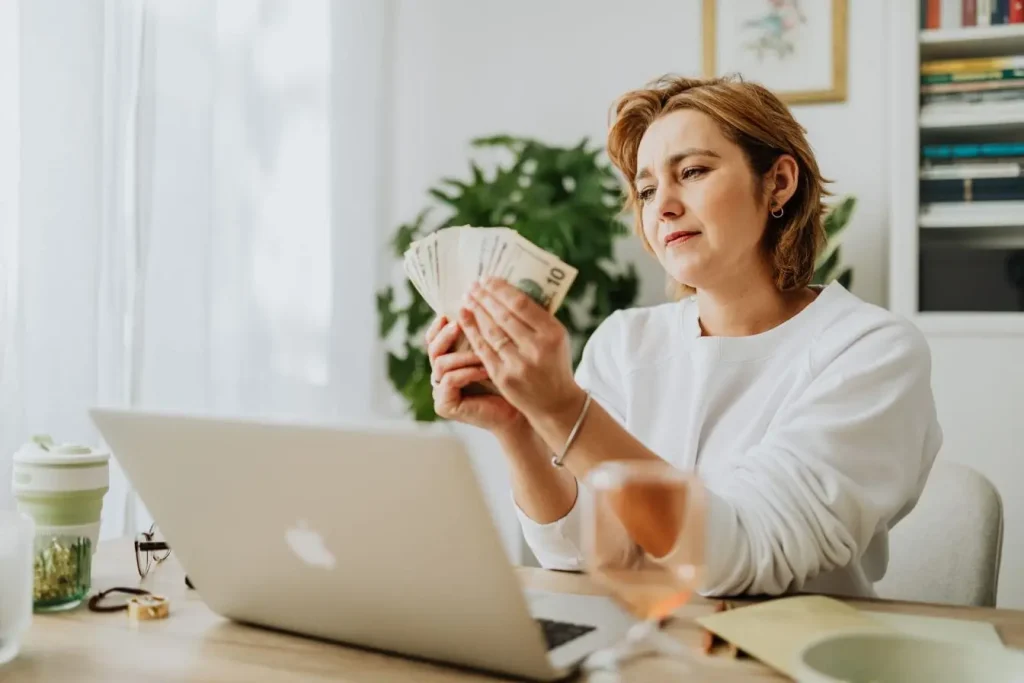 Personne comptant des billets devant ordinateur portable, image illustrant le bootstrapping et l’autofinancement d’un projet entrepreneurial.