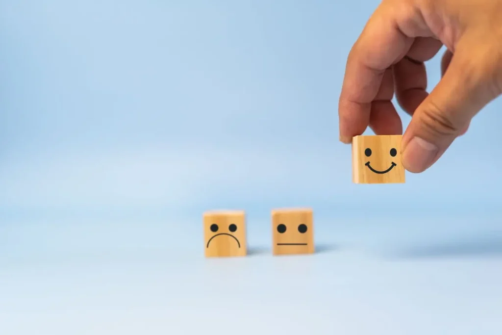 Trois cubes avec visages triste neutre et heureux, une main choisit le sourire, image d’un marketing basé sur consentement et choix positif du client.