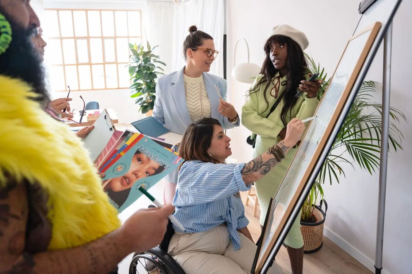 Groupe de quatre personnes en bureau moderne collaborant autour d’un tableau blanc, illustrant un atelier pour mesurer la notoriété d’une marque.