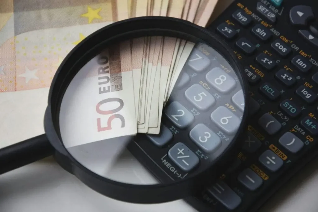 Billets et calculatrice sous loupe, image d’un travailleur indépendant qui ajuste ses tarifs pour équilibrer effort et rémunération.