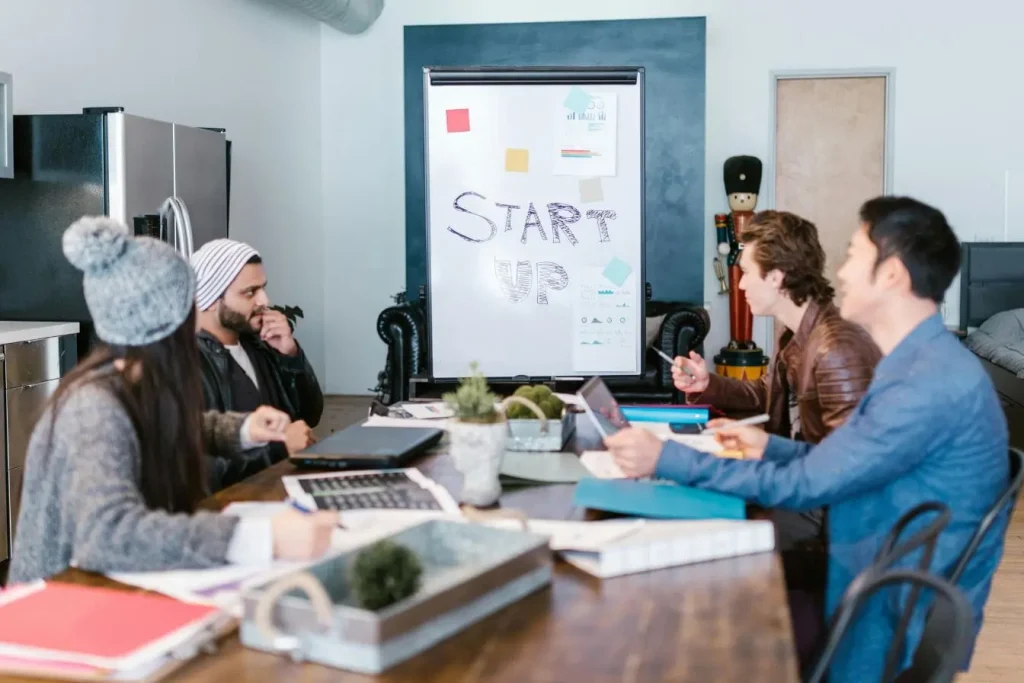 Quatre personnes réunies autour d’une table avec ordinateurs et dossiers, image illustrant le pivot en startup lors d’une réunion stratégique.