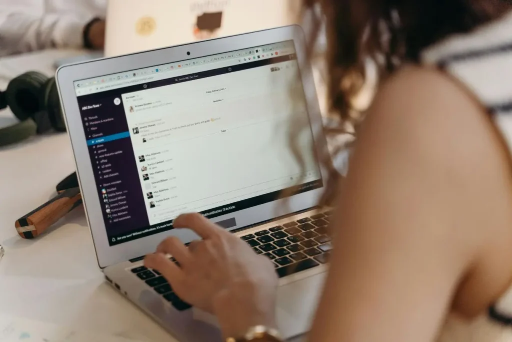 Personne utilisant ordinateur portable affichant Slack, illustrant la dynamique de créer une communauté en ligne et favoriser l’échange collaboratif.