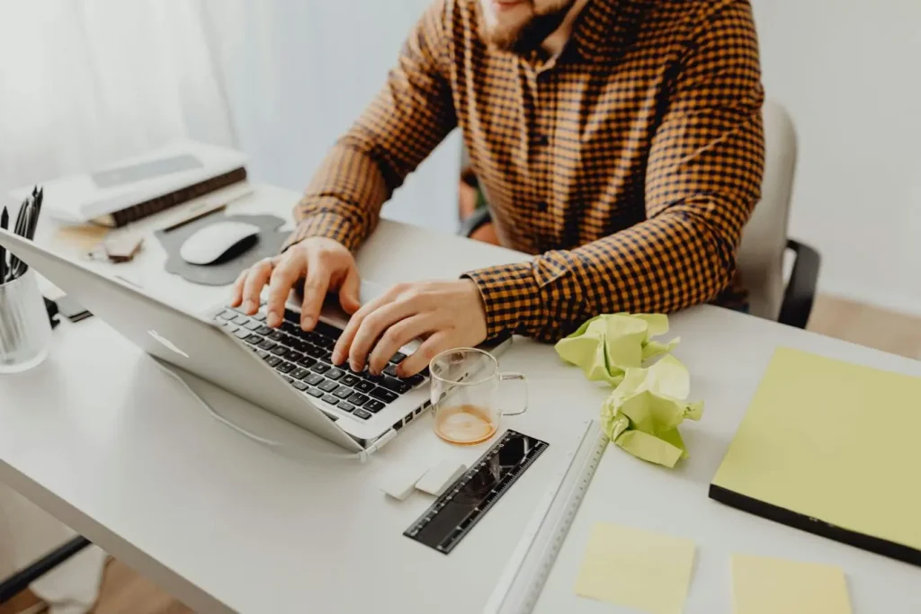 Personne en chemise orange et noire travaillant sur laptop, image illustrant les efforts pour décrocher ses premiers clients en freelance.
