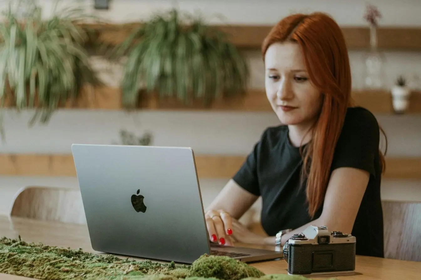 Personne aux cheveux roux travaille sur ordinateur portable, image d’un freelance qui réfléchit à la meilleure façon de fixer ses tarifs.