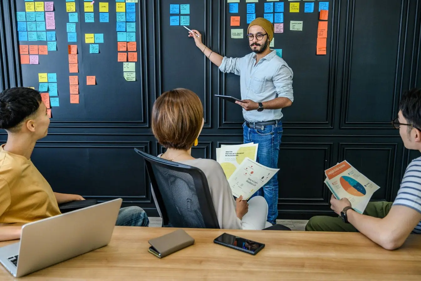 Personne debout devant mur rempli de post-it colorés, image illustrant le rôle du Product Owner guidant l’équipe.