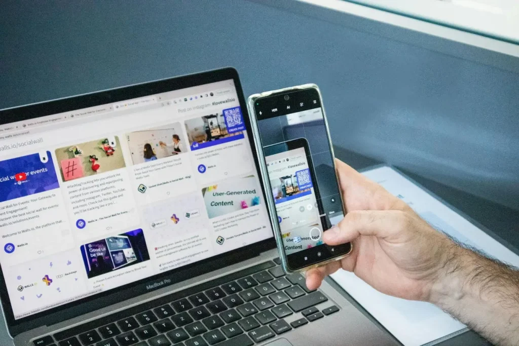Personne tenant un smartphone devant un ordinateur affichant une plateforme sociale, illustrant la visibilité réduite du shadow ban.