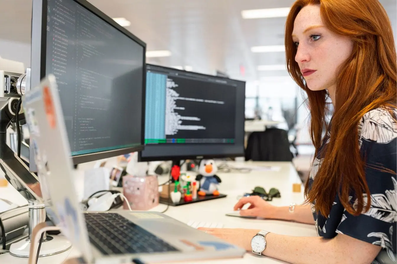 Développeur travaille sur double écran affichant code, image illustrant les pratiques DevOps en environnement moderne.
