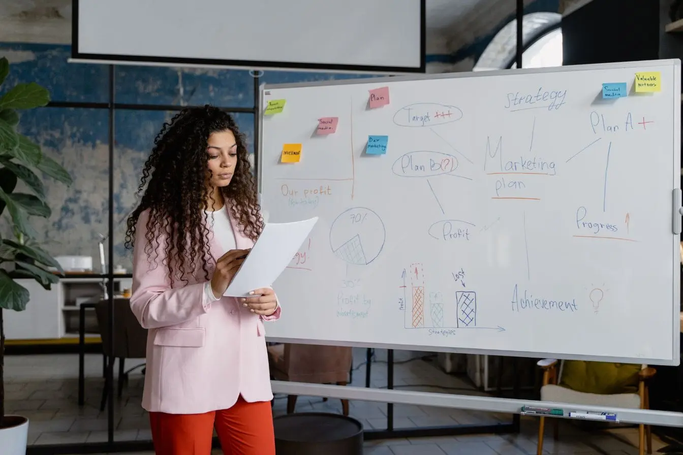 création d’un pitch deck Personne en chemise présente devant tableau rempli de notes colorées, image illustrant la création d’un pitch deck structuré.