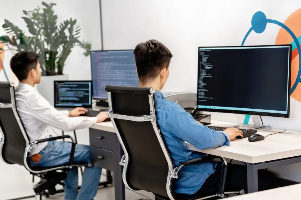 Deux développeurs concentrés devant écrans affichant code, image illustrant la distinction entre conception UX et design UI.