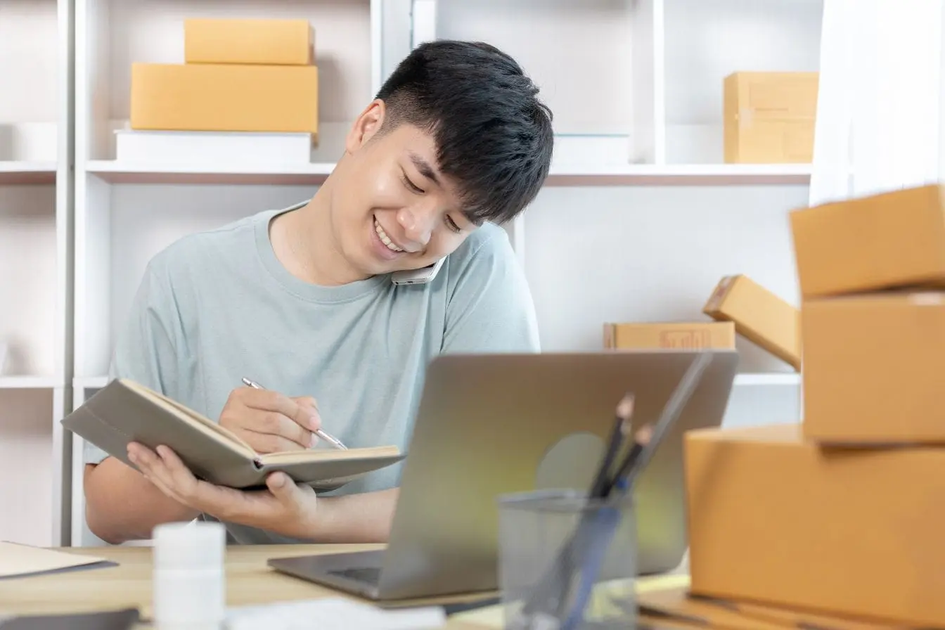 dropshipping Personne au bureau tenant un carnet et parlant au téléphone reflétant la vigilance et la discipline nécessaires pour gérer une activité de dropshipping.