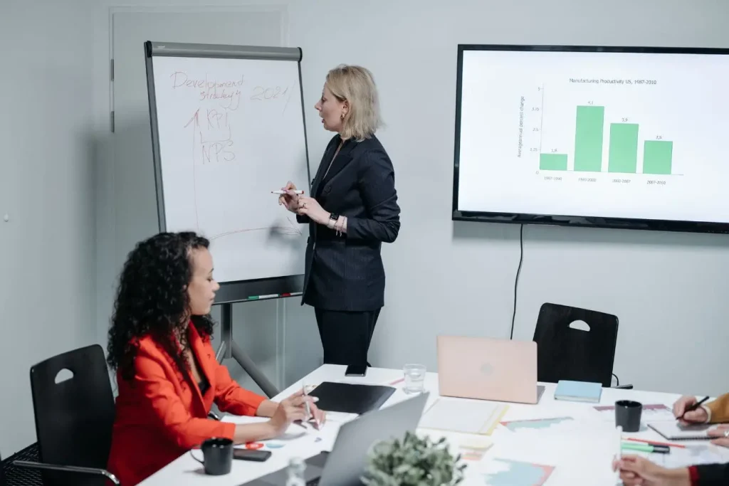 Personne présente stratégie devant tableau avec graphiques et indicateurs, image illustrant la création d’un pitch deck clair et structuré.