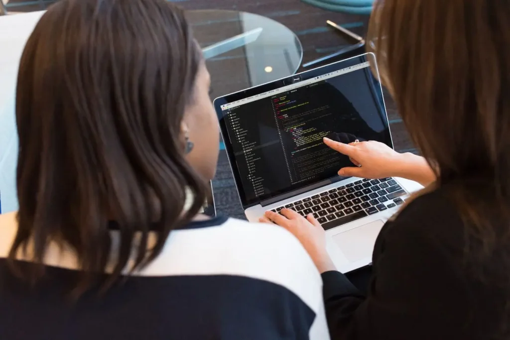 Deux personnes collaborent devant écran affichant code, image illustrant la culture DevOps et le travail d’équipe en développement logiciel.