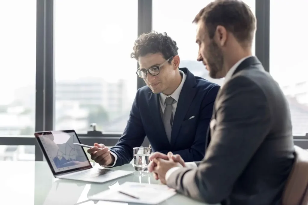 Deux personnes en tenue professionnelle analysent un graphique sur laptop, image qui illustre la recherche du Product-Market Fit.