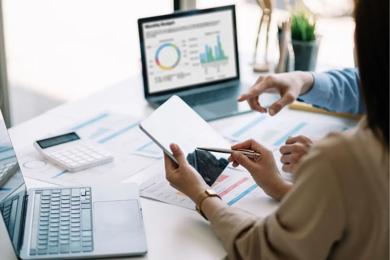 Deux personnes analysant graphiques sur table avec ordinateurs, image qui illustre la pratique de la veille concurrentielle pour orienter les décisions.