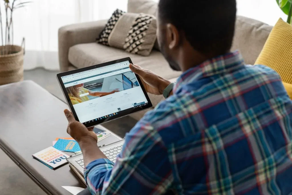 Personne assise sur canapé utilisant une tablette affichant LinkedIn Sales Navigator, image qui illustre le recrutement moderne via LinkedIn.