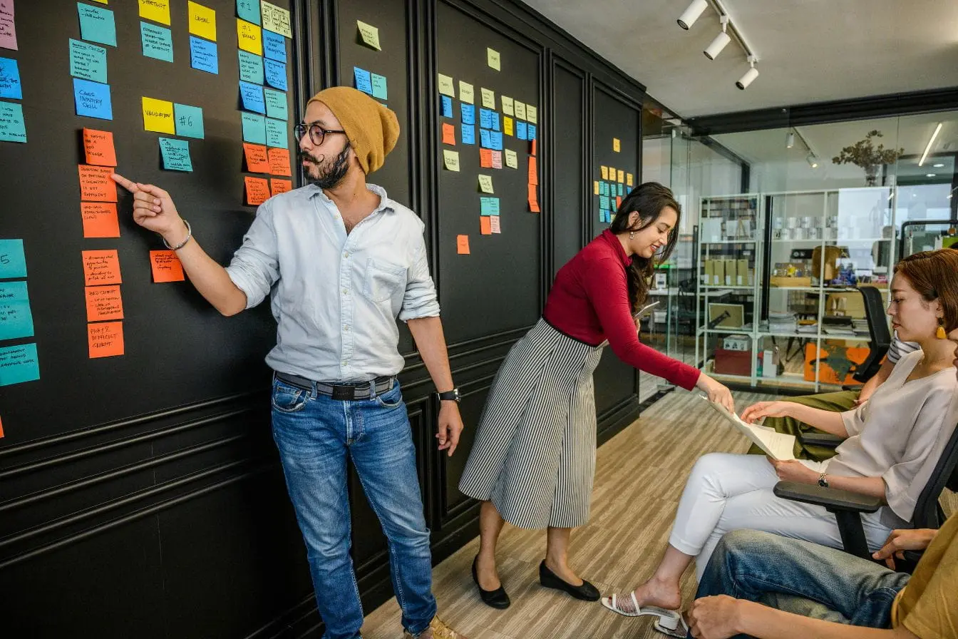 Scrum Master Équipe réunie autour d’un mur couvert de post-it colorés, image qui illustre le rôle du Scrum Master dans l’organisation agile.