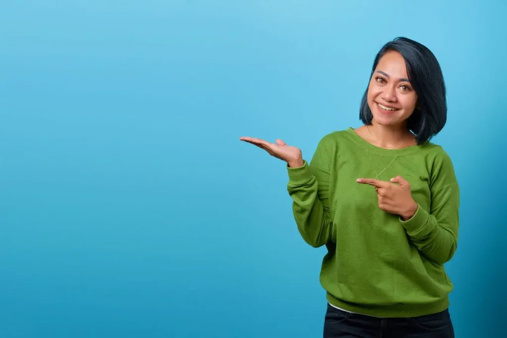 Personne souriante en chemise verte pointant sa main ouverte, image claire d’une communication visuelle respectant la brand safety.