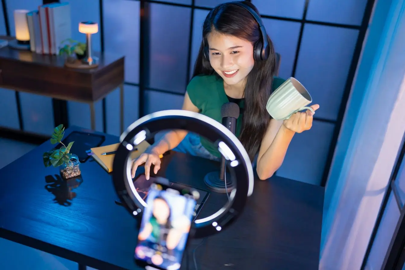 Personne assise à bureau avec casque et micro, smartphone sur trépied éclairé par ring light, reflet d’une création de snack content dynamique.