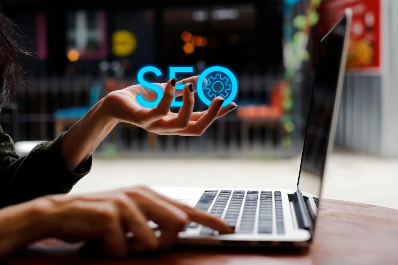 Personne utilisant un ordinateur portable avec hologramme bleu SEO, image qui illustre l’importance du référencement vocal pour optimiser la visibilité en ligne.