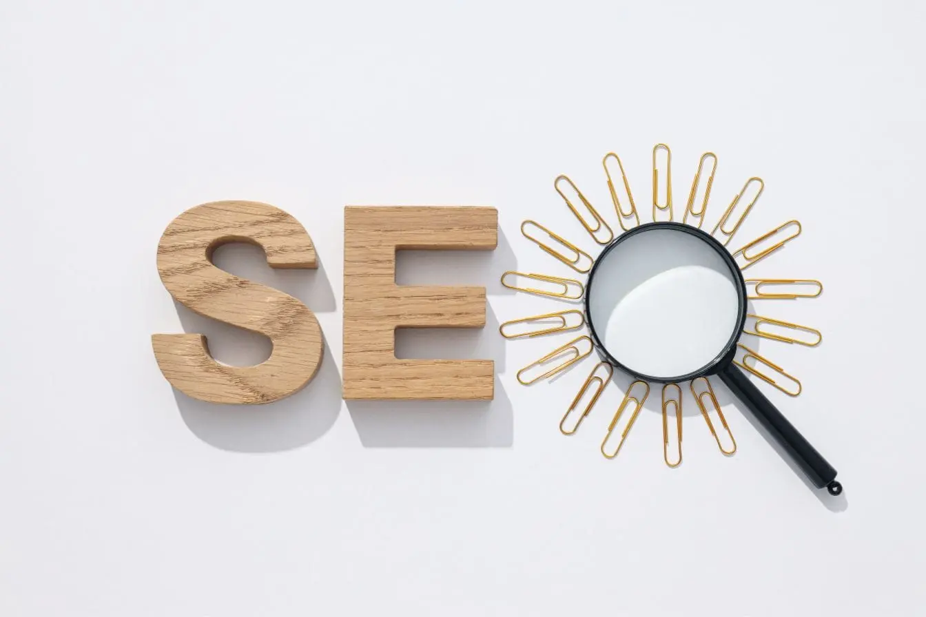 Lettres en bois S et E posées sur fond blanc avec loupe et trombones dorés, reflet des signaux SEO clés de 2026.