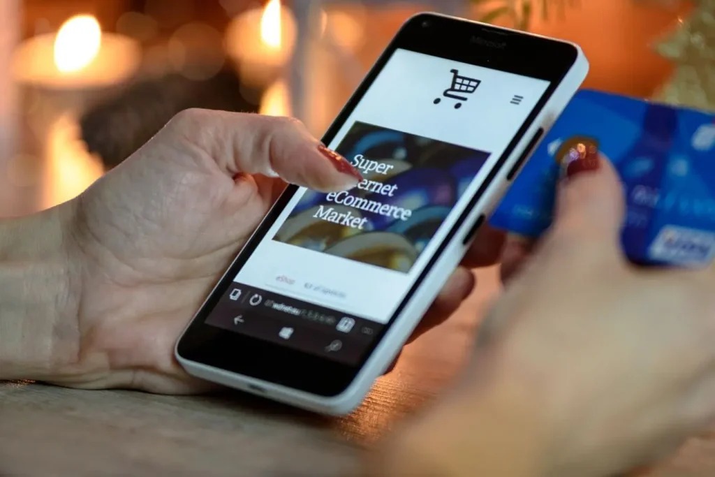 Gros plan sur main tenant smartphone affichant site e‑commerce et carte bancaire, reflet d’une gestion de budget crawl.