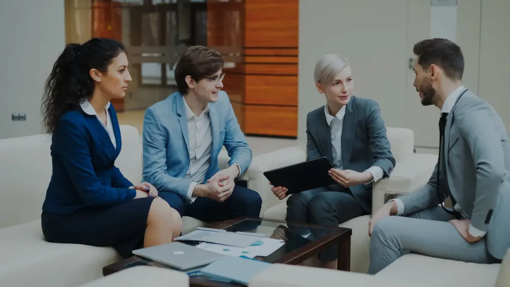 Quatre professionnels en costumes discutant autour d’une table vitrée, reflet des stratégies de personal branding sur LinkedIn.