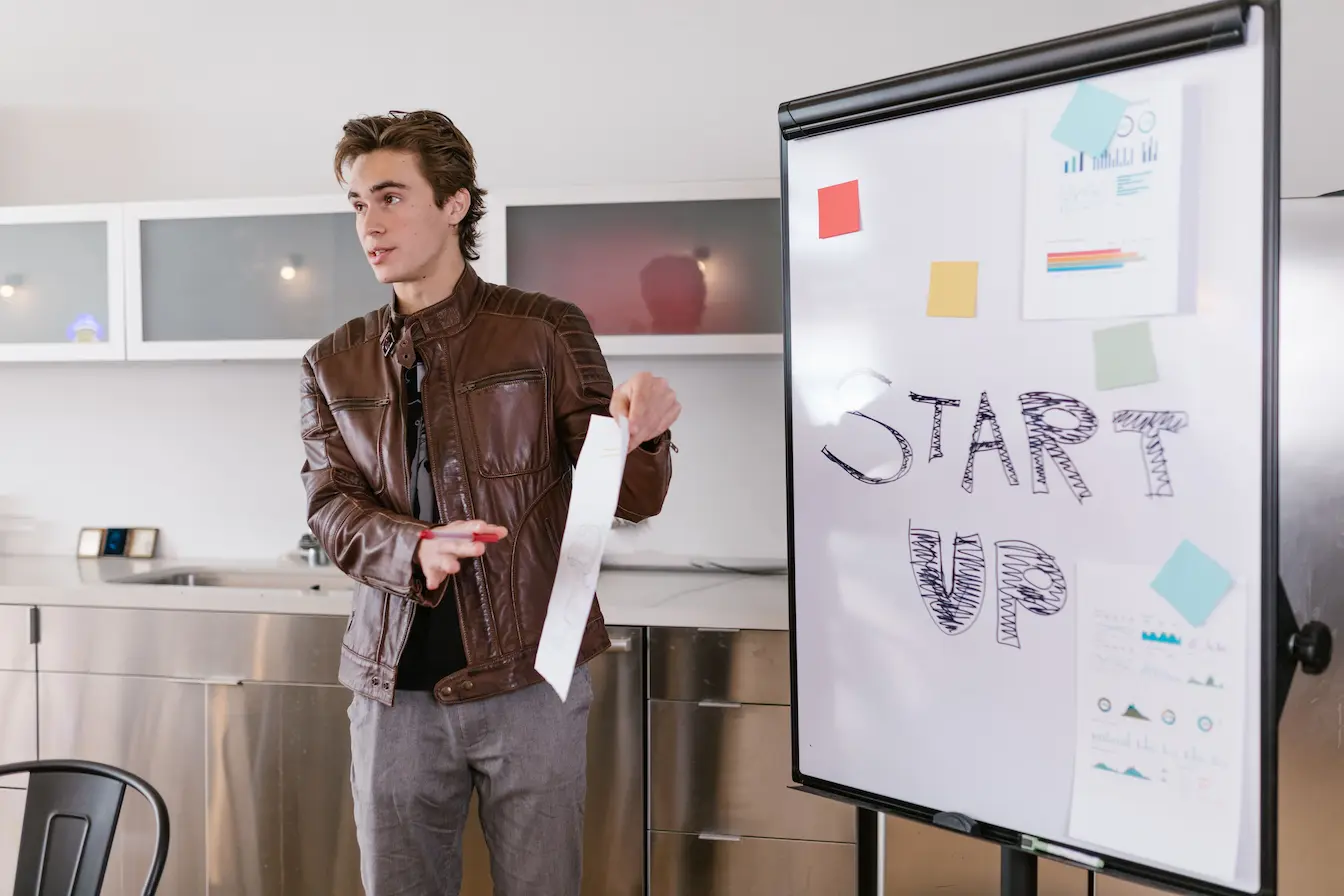 Personne en veste cuir présentant devant tableau START UP, symbole des choix de financement entre Business Angel et Venture Capital pour une startup.