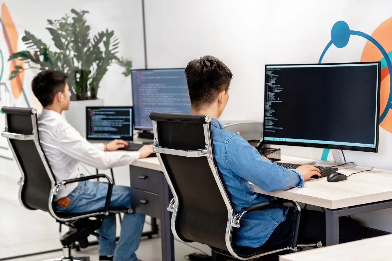 DevOps Deux développeurs travaillent sur plusieurs écrans affichant du code source, illustrant la collaboration continue entre développement et exploitation en mode DevOps