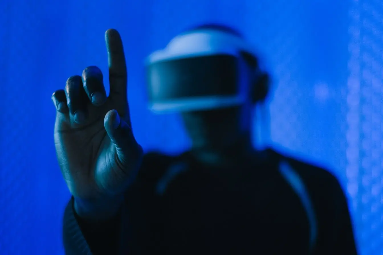 Métavers Une personne portant un casque de réalité virtuelle tend la main pour interagir dans le métavers sous une lumière bleue immersive.