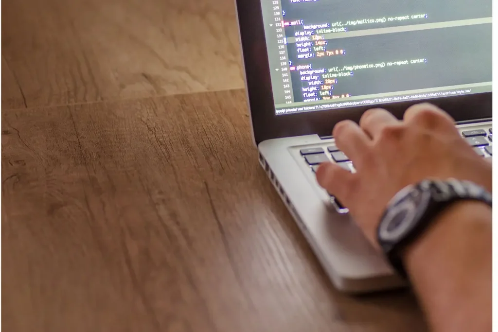 Main posée sur clavier d’ordinateur portable affichant code CSS, symbole du travail technique autour des API REST.
