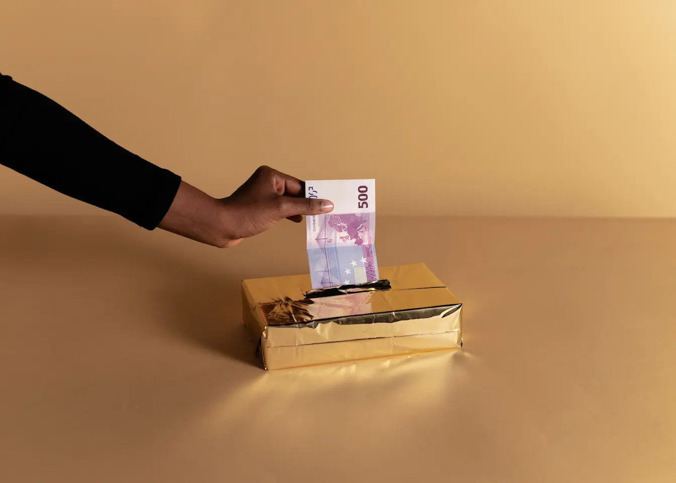 levée de fonds Main insérant billet de 500 euros dans boîte dorée, symbole des étapes clés d’une levée de fonds réussie.