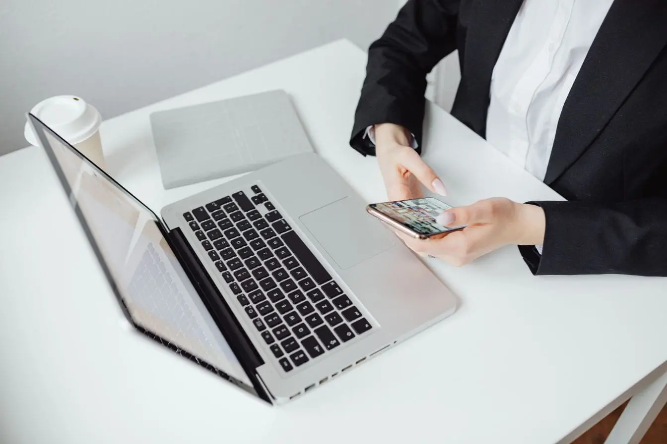 métriques SaaS Personne en costume assise à bureau blanc utilisant smartphone et ordinateur portable, symbole des métriques SaaS essentielles à suivre pour la productivité.