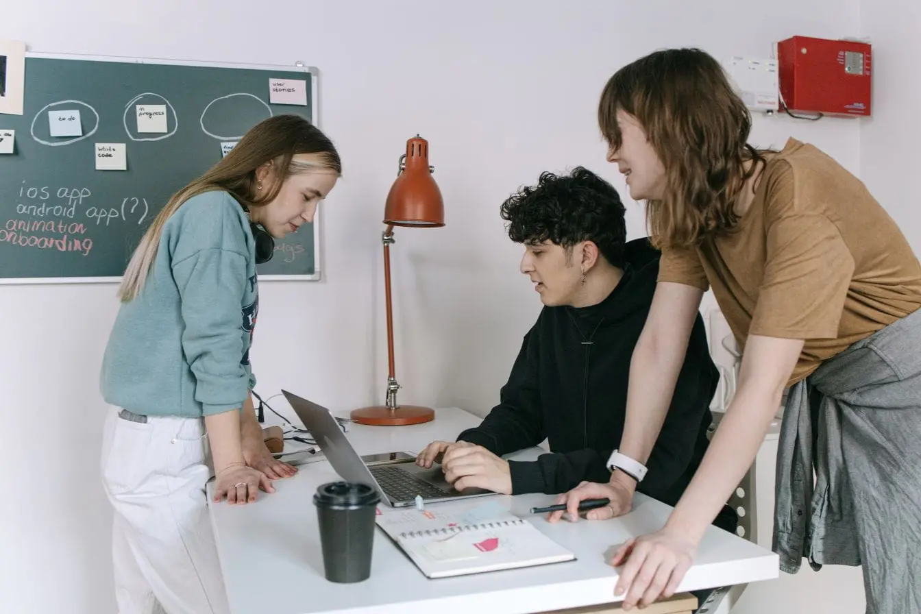onboarding utilisateur Trois personnes réunies autour d’un bureau avec ordinateur portable, symbole des étapes d’onboarding utilisateur en projet numérique.