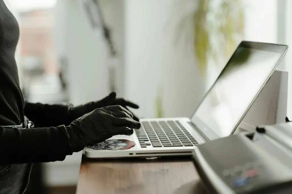 Une personne portant des gants noirs tape sur le clavier d'un ordinateur portable pour symboliser une fraude par phishing.