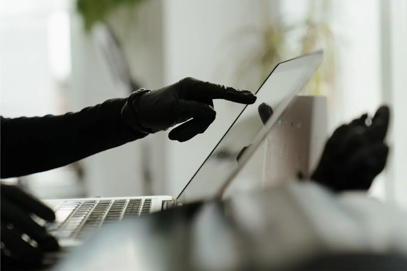 phishing Une personne portant des gants noirs tape sur le clavier d'un ordinateur portable pour illustrer une tentative de phishing.