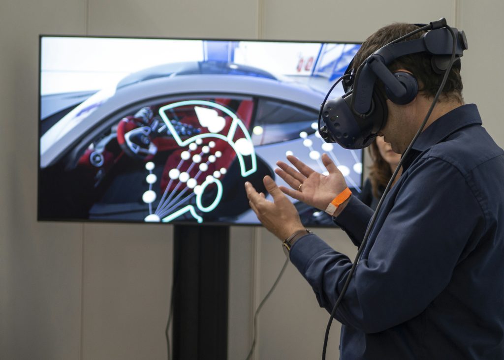 Homme équipé d'un casque de réalité virtuelle face à un écran affichant l'intérieur 3D d'une voiture