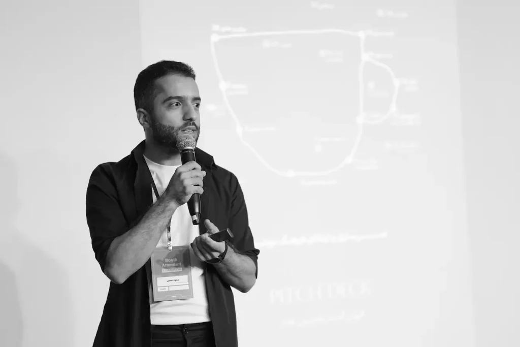 Personne tenant micro devant diapositive projetée, symbole d’une présentation pitch deck en événement professionnel.